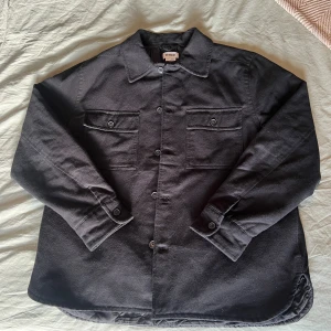 Svart quiltad overshirt från Weekday - Svart overshirt från Weekday i storlek M med quiltat foder på insidan. Skjortan har två bröstfickor med knappar, klassisk krage och knäppning framtill. Materialet är mjukt och slitstarkt, perfekt för lager-på-lager. Snygg loose passform och långärmad design.