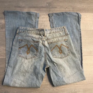 Ljusblå bootcut jeans med broderi - Säljer ett par ljusblå jeans med bootcut passform och snyggt brunt broderi på bakfickorna. Jeansens mått : midjemått 37 cm tvärs över, innerbenslängd 71 cm, benöppning 25 cm