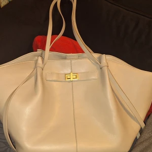 Beige axelväska från Gina Tricot - Jätte snygg beige axelväska från Gina Tricot i slätt syntetmaterial. Väskan har långa smala axelband och snygg guldfärgad vridknäppe framtill. Rymlig stor modell med long stramp design. Lite slitna handtag och små fläckar på insidan men det är inget som man tänker på 💕