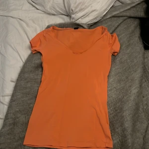 Orange t-shirt från G-Star RAW - Säljer en orange t-shirt från G-Star RAW med v-ringning och korta ärmar. Toppen har en broderad logga på bröstet och är i ett mjukt, stretchigt material som sitter snyggt på kroppen. Perfekt för dig som gillar färg och enkel stil.