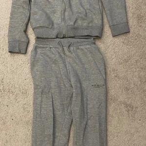 Grå set från McKenzie - Grå set från McKenzie med snörning i midjan och tryckt logga på benet. Sköna och avslappnade med normal passform, perfekta för chill eller träning. Tillverkade i mjukt bomullsmaterial för extra komfort.