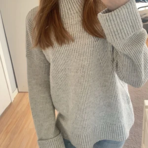 Grå stickad polotröja Pernilla Wahlgren - Supermysig grå stickad polotröja från Pernilla Wahlgren Design. Tröjan har ribbad struktur, hög polokrage och långa ärmar med breda muddar. Perfekt för lager på lager och chill dagar. Snygg till både jeans och kjol.