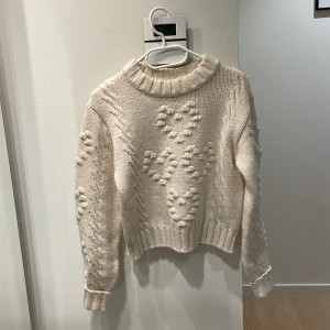 Beige stickad tröja m. hjärtmönster | Monki - Supermysig beige stickad tröja från Monki i storlek S. Tröjan har ett upphöjt hjärtmönster framtill, grovstickad struktur och bred ribbad mudd vid hals, ärmslut och nederkant. 🤍❄️