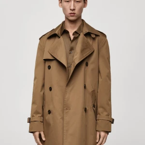 Beige trenchcoat med bälte - Snygg beige trenchcoat från Mango med klassisk dubbelknäppning, axelklaffar och bälte i midjan. Jackan har långa ärmar med spännen vid mudden och två framfickor. Perfekt för dig som gillar stilrena och tidlösa plagg.