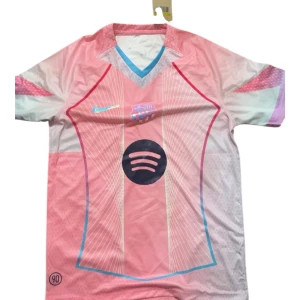 Rosa FC Barcelona fotbollströja Nike - Säljer en unik rosa FC Barcelona fotbollströja från Nike med Spotify-logga på bröstet. Tröjan har korta ärmar, V-ringad krage med blå och grå detaljer samt tunna vita linjer och grafiska mönster. Perfekt för dig som gillar färgstarka och moderna sportplagg.