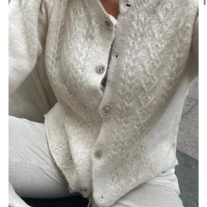 Beige stickad kofta från Design by Si - Superfin beige stickad kofta från Design by Si med snyggt mönster framtill och rund hals. 