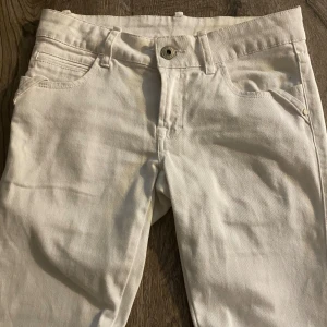 Vita jeansbyxor från Gina, stl 28 - Snygga vita jeansbyxor från Gina i klassisk femficksmodell. Byxorna är Boot Cut, knäppning med knapp och dragkedja samt bakfickor med lock och knapp. Perfekta för dig som gillar stilrena och ljusa jeans.
