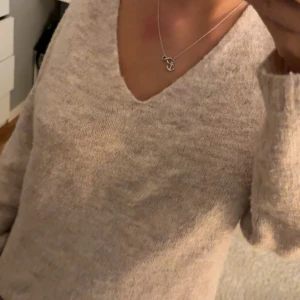 Beige stickad v-ringad tröja - Mysig beige stickad tröja med v-ringning och långa ärmar. Tröjan har en enkel och stilren design som passar perfekt till jeans eller kjol. Den är mjuk och skön, perfekt för kyligare dagar.