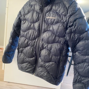 Marinblå cloud dunjacka Peak Performance - Säljer en marinblå dunjacka från Peak Performance med vågformat quiltat mönster, cloud. Jackan har dragkedja framtill och två sidofickor med dragkedja. Perfekt för kalla dagar och riktigt snygg till streetwear. Mindre skada på ena ärmen. Frakt betalas av köpare.