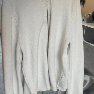 Beige stickad kofta från Gina Tricot - Säljer en beige stickad kofta från Gina Tricot i storlek XS. Koftan har långärmade ärmar, ribbade detaljer vid hals och muddar samt en knapp framtill. Säljer för den inte används🩷