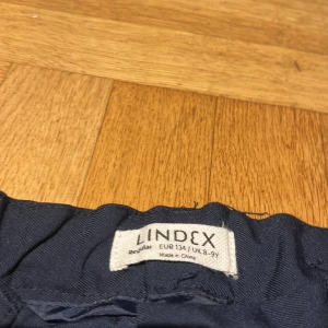 Mörkblå kostymbyxor från Lindex - Snygga mörkblå kostymbyxor från Lindex med rak passform och klassiska fickor. Byxorna har knapp och hällor för bälte i midjan, vilket ger en stilren look. Perfekta för dig som gillar enkel och clean stil.