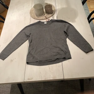 Grå basic tröja från Lindex - En enkel och stilren grå tröja från Lindex med rund halsringning och långa ärmar. Tröjan är i mjukt material och har ribbade muddar vid hals, ärmslut och nederkant. Perfekt för lager-på-lager under kyliga dagar.