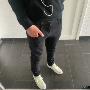 Svarta Replay Anbass jeans, stl 31/32 - Säljer ett par svarta Replay Anbass jeans i storlek 31/32. De har en slim passform med klassisk femficksdesign och dragkedja. Snygg, enkel look som funkar till det mesta. Materialet är mjukt och stretchigt för extra komfort.