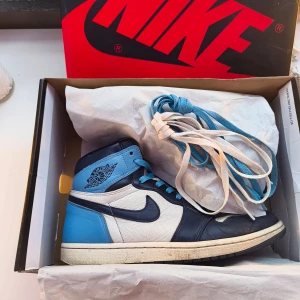 Jordan 1 Retro High Obsidian strl 44 – Använt skick - Air Jordan 1 Retro High OG Obsidian i storlek 44, säljes i använt skick med slitningar på hälen (se bilder). Originalkartong och extra skosnören ingår. Populär och eftertraktad färgkombination för dig som vill ha ett par äkta Jordans till bra pris. 