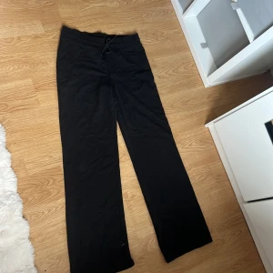 Svarta mjukisbyxor med snörning - Svarta mjukisbyxor med rak passform och snörning i midjan. Byxorna är tillverkade i mjukt material och har en avslappnad look, perfekta för chill dagar eller när du vill vara bekväm. Klassisk design utan synliga loggor eller detaljer.