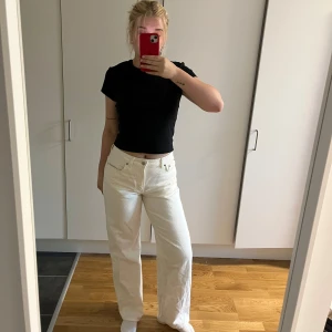 Vita raka jeans med hög midja - Säljer ett par vita jeans med hög midja och raka ben. Byxorna har klassisk femficksdesign och stängs med knapp och dragkedja. De är tillverkade i ett stadigt bomullstyg och har en clean, stilren look som är lätt att matcha. Använda en gång