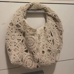 Beige virkad axelväska - Superfin beige axelväska med virkat mönster och rundad form. Väskan har ett unikt, handgjort utseende med detaljerade blommiga virkade partier och ett mjukt innerfoder. Perfekt för dig som gillar boho-stil och vill sticka ut🤎