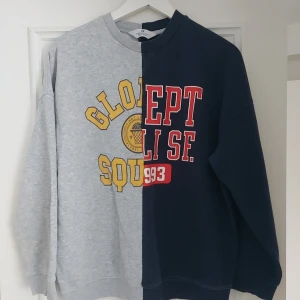 Tvåfärgad college-tröja från H&M ,storlek 14-15år - Säljer en unik sweatshirt från H&M med coolt delad design i grått och mörkblått. Tröjan har tryck i gult och rött framtill, rund hals och långa ärmar. Perfekt för dig som vill sticka ut med en sportig och trendig look.