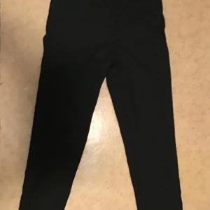 Svarta kostymbyxor från H&M - Svarta kostymbyxor från H&M i klassisk rak modell. Byxorna har dragkedja och knapp framtill samt justerbar midja på insidan. Perfekta för en clean och stilren look. Materialet är mjukt och följsamt, vilket gör dem bekväma att bära hela dagen.