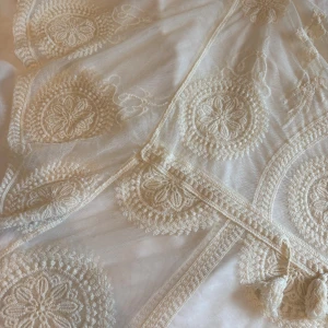 Vit broderad boho-klänning med tofsar - Superfin vit klänning i boho-stil med broderade blommönster och transparent mesh. Bad klänning till stranden som är genomskinlig 