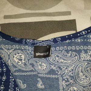 Blå mönstrad blus från Gina Tricot - Säljer en blå långärmad blus från Gina Tricot i storlek L. Toppen har ett paisleyinspirerat mönster i vitt och blått, v-ringad hals och figurnära passform. Perfekt för dig som gillar unika prints och vill sticka ut lite extra.