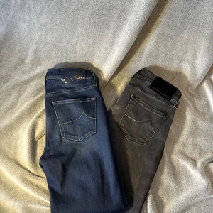 Jacob Cohën jeans i blått och grått - Två par snygga Jacob Cohën jeans, ett i klassiskt blått och ett i mörkgrått. Båda har tydliga bakfickor med kontrastsömmar och exklusiv logotyp-patch bak i midjan. Tillverkade i mjukt denimtyg med dragkedja och unika detaljer invändigt. 1par = 439kr 2 par = 799