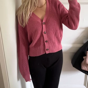 Rosa kofta från Gina Tricot - Superfin rosa kofta från Gina Tricot i stickad bomull. Modellen är croppad med v-ringning och har snygga knappar framtill. Perfekt att slänga på sig när det är lite kyligt. Passar dig som gillar en loose fit och vill ha en chill look. 