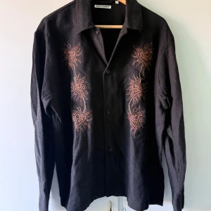 Our Legacy - Skjorta - 48 - Svart skjorta med brodyr från Our Legacy. Den är helt ny, har aldrig använt den. Vill helst att köpt vara hämtas på Södermalm i Stockholm.