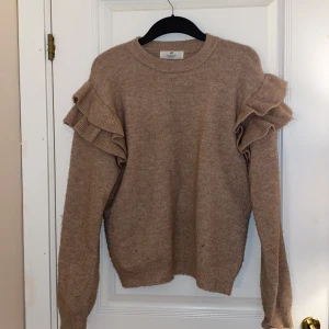 Beige stickad tröja med volang H&M - Superfin beige stickad tröja från H&M med volangdetaljer på axlarna. Tröjan har rund halsringning och långa ärmar, perfekt för dig som vill ha något mysigt men ändå trendigt. Passar dig som gillar en lite loose fit och vill sticka ut med snygga detaljer.perfekt färg och stil inför hösten! Väldigt skönt material.