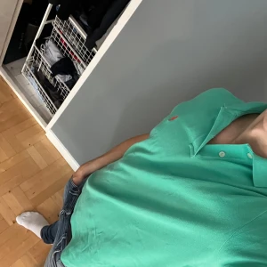 Grön pikétröja från Ralph Lauren M - Snygg grön pikétröja från Ralph Lauren i klassisk passform. Tröjan har korta ärmar, krage med knappar och den ikoniska röda loggan broderad på bröstet. Tillverkad i 100% bomull, perfekt för en chill och stilren look.