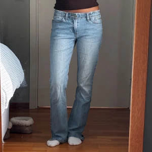 Ljusblå bootcut jeans med slits - Snygga ljusblå jeans med bootcut passform och liten slits nertill på benen. Klassisk femficksmodell med orange sömmar och knappgylf. Jeansen har låg midja och är tillverkade i äkta denim för en tidlös look. Från Brandy Melville. Jag har sytt ett resårband i midjan så det ska sitta tajt men är jättelätt att ta bort. 
