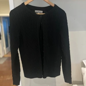 Svart kofta från Basic You i bomull - Använd väldigt få gånger. Men som ny i skicket. Svart kabelstickad kofta från Basic You i ekologisk bomull. Klassisk rund halsringning, knäppning framtill med svarta knappar och långärmad modell. Perfekt att slänga över en t-shirt eller linne för en chill look. 🥰🥰