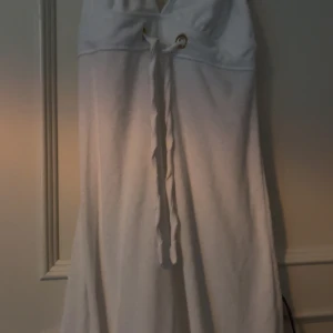 Vit långklänning med snörning - Vit långklänning med djup v-ringning och snörning baktill. Klänningen är ärmlös och har en öppen rygg. 