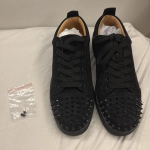 Christian Louboutin - Svarta sneakers från Christian Louboutin med coola svarta nitar på tån. Skorna har snörning och är tillverkade i mocka med skinnfoder. Kommer med originalkartong, dustbag och kvitto. Perfekta för dig som vill sticka ut med en edgy och lyxig stil. Jag kan inte garantera äktheten av denna vara. Kan skicka bild på allt, det bara att be om det. Sänker pris vid snabb affär