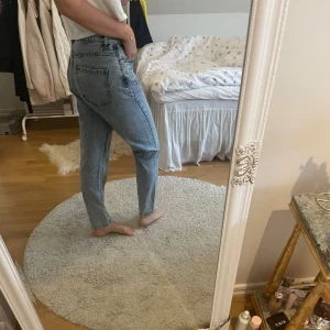 Blå högmidjade raka jeans - Säljer ett par klassiska blå jeans med hög midja och raka ben. Jeansen har fem fickor, dragkedja och knapp framtill. Perfekta för dig som gillar en tidlös och avslappnad stil. Materialet är robust denim som håller formen hela dagen.