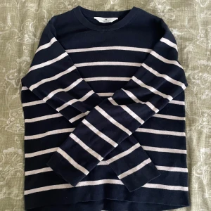 Mörkblå randig tröja från H&M - Snygg mörkblå tröja från H&M med vita horisontella ränder. Klassisk rund hals och långa ärmar, perfekt för dig som gillar enkel och stilren design. Materialet är mjukt och skönt bomull, passar dig som vill ha en chill och tidlös look.
