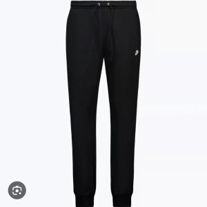 Svarta mjukisbyxor från Nike - Svarta mjukisbyxor från Nike med klassisk logga på låret. Byxorna har dragsko i midjan och muddar vid bensluten för en skön passform. Perfekta för chill eller träning, tillverkade i mjukt material.