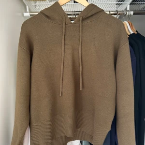 Olivgrön stickad hoodie med huva - Säljer en olivgrön stickad hoodie med huva och snörning. Tröjan har ribbade muddar och nederkant, samt lång ärm. Perfekt för dig som gillar en enkel och stilren look med en avslappnad passform. färgen är kahki men syns dåligt på bild
