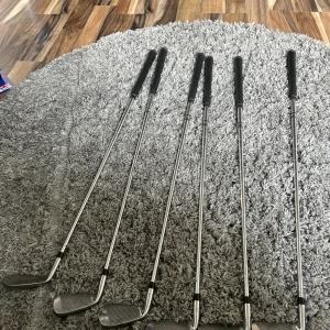 Set med 5 st golfklubbor SP98 - Säljer ett set med fem golfklubbor från SP98. Klubborna har svarta grepp, silverfärgade skaft i metall och klubbhuvuden i silver med svarta och röda detaljer. Perfekt för dig som vill börja spela golf eller behöver extra klubbor till samlingen.