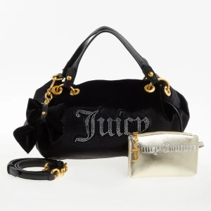 Juicy Couture primerose sammetshandväska - Svart primerose handväska / axelväska i sammet från Juicy Couture med glittrande Juicy-logga framtill, guldfärgade metalldetaljer, avtagbar axelrem och dekorativ rosett. Medföljer en liten metallic-guldfärgad necessär med Juicy Couture-tryck. Perfekt för dig som gillar statement-accessoarer. Cirkamått i cm på väskan: 30x24x20 och på plånboken: 14x9x2. Ny med etikett.