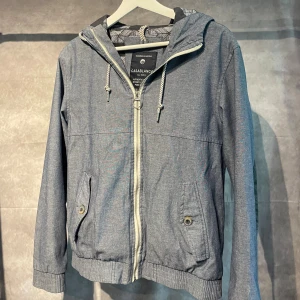 Casablanca Windbreaker - Snygg grå vindjacka från Casablanca med huva och dragsko, mönstrat innerfoder och dragkedja framtill. Jackan har ribbade muddar, fickor med knapp och svarta förstärkningar på armbågarna. Perfekt för dig som gillar stilren och sportig look.