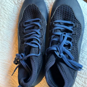 Blå sneakers från Puma med stickad ovandel - Säljer ett par snygga blå sneakers från Puma med stickad ovandel och matchande blå snörning. Skorna har en sportig look med rund tå och platt sula, samt Pumas logga på sidan och under sulan. Perfekta för dig som gillar stilrena och bekväma sneakers.