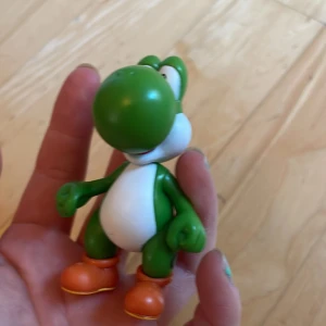 Yoshi figur - Söt Yoshi-figur från Nintendo, perfekt för samlare eller fans av Super Mario. Figuren är i gott skick med fina färger och detaljer. Inga synliga skador eller större slitage. Märkt med CE och serienummer under foten.