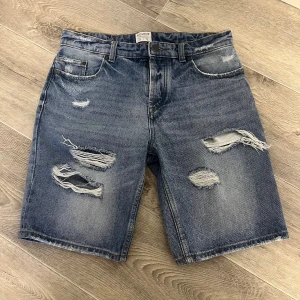Blå slitna jeansshorts Pull&Bear - Snygga blå jeansshorts från Pull&Bear med slitna detaljer och råa kanter. Klassisk femficksmodell med normal passform och knappgylf. Perfekta för en avslappnad stil under varma dagar.