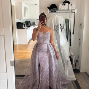 Ljuslila glittrig balklänning/festklänning - Säljer en magisk ljuslila långklänning med glittriga detaljer och sweetheart-urringning. Klänningen är axelbandslös och har en snygg slits framtill. Perfekt för bal eller festliga tillfällen. Den fluffiga delen av kjolen är även avtagbar så man får en tight långklänning. Köpt på Facebook market men användes aldrig då jag valde en annan klänning istället, aldrig använd av mig och endast använd 1 gång av ägaren innan