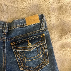Blå bootcut jeans från Gina Tricot - Snygga blå jeans från Gina Tricot, modell Perfect Jeans. De har låg midja och bootcut-ben, med klassiska fickor och coola kontrastsömmar. Jeansen är i denim med en mörkare tvätt och passar perfekt till en trendig vardagslook.