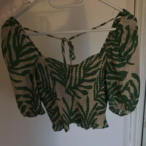 Grönmönstrad croppad blus med puffärm - Säljer en croppad blus med grönt och beige zebramönster. Toppen har puffiga trekvartsärmar, smockad midja och knytning i ryggen. 