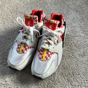 Nike Air Huarache Liverpool FC edition - Unika Nike Air Huarache sneakers i Liverpool FC edition med röd och vit rutig design, gula och svarta detaljer. Skorna har vit bas, röda inslag och klassisk snörning. De är väldigt sparsamt använda och är som nya. Tydlig Nike-logga baktill och Liverpool FC-märke framtill . Du får även med andra kardborredetaljer, du kan byta den främre till Nike air hurrache detalj och den bakre till YNWA. (Se bild 5) strl eur 42,5