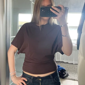 Brun croppad topp med kort ärm - Säljer en brun croppad topp med korta ärmar och rund hals. Toppen har en tight passform över midjan och är tillverkad i ett mjukt bomullsmaterial. Perfekt att styla med jeans eller kjol för en chill look.