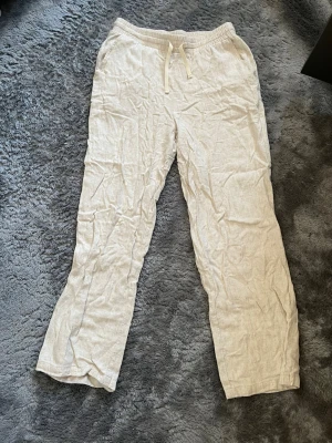 Beiga linnebyxor från Grunt - Säljer ett par beiga linnebyxor från Grunt i storlek L. Byxorna har resår och dragsko i midjan för skön passform och är tillverkade i ett luftigt linnematerial. Perfekta för en avslappnad och stilren look.